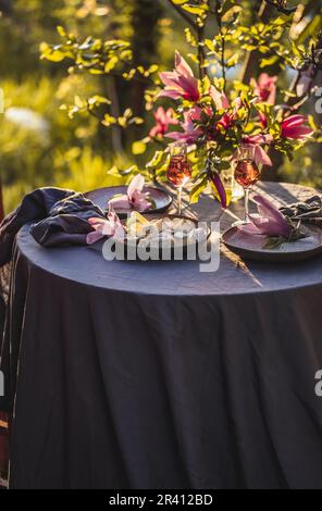 Table Setting in Garden on Sunset Light. Table decorated with magnolia flowers under magnolia tree. Stock Photo