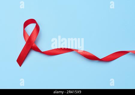 A silk red ribbon in the form of a bow is isolated on a blue background, a symbol of the fight against AIDS and a sign of solida Stock Photo