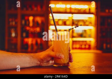 Crystal glass with orange cocktail and sprig of lavender on a bar blurred background. Free space for text Stock Photo