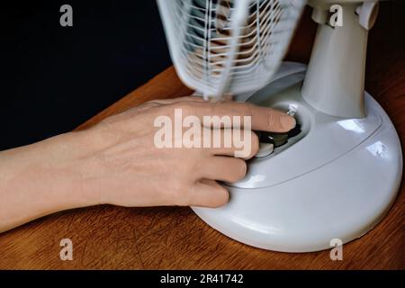 close-up of a person using a household fan. a female hand regulates the temperature of an electric fan. Stock Photo
