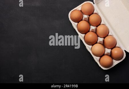 Raw brown chicken eggs in a paper cardboard container on a black background, top view Stock Photo