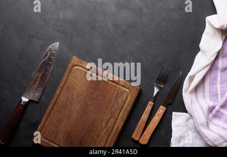 Empty wooden kitchen cutting board, knife and fork with wooden handle on black background, top view Stock Photo