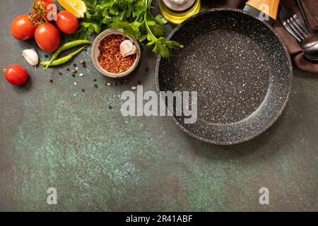 Food cooking background with Frying pan. Empty skillet, vegetables, spices and herbs on dark table background. View from above. Stock Photo