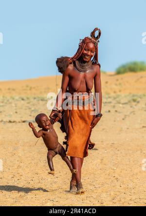 Himba woman is carrying her child, holding his hand. Stock Photo