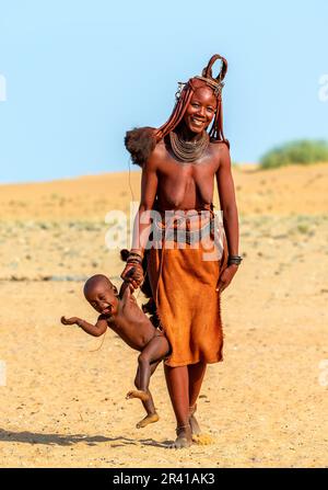 Himba woman is carrying her child, holding his hand. Stock Photo