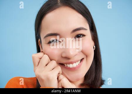 Close up portrait of beautiful japanese brunette girl, smiling and looking lovely at camera, gazing with care and tenderness, bl Stock Photo