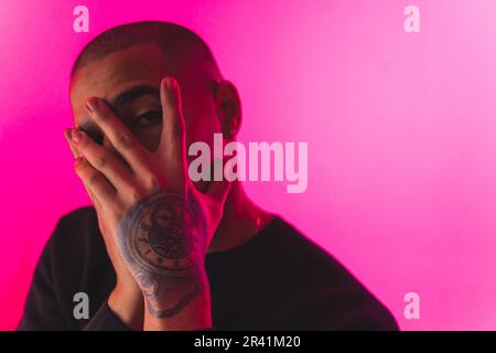 Young Afro-American guy hiding his face with tattooed hands peeks through fingers. Depression or fear concept. High quality 4k footage Stock Photo