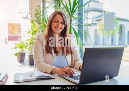Happy businesswoman working online in office using laptop. Smiling middle-aged woman looking at camera sitting at desk Stock Photo
