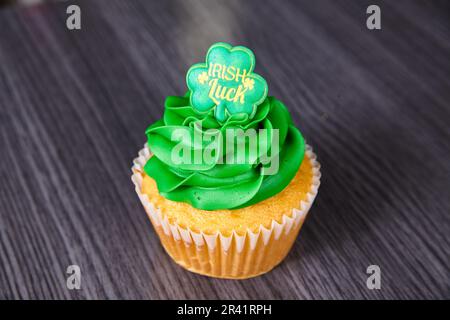 Vanilla St. Patrick’s Day cupcake green frosting Irish Luck four-leaf clover topper simple background Stock Photo