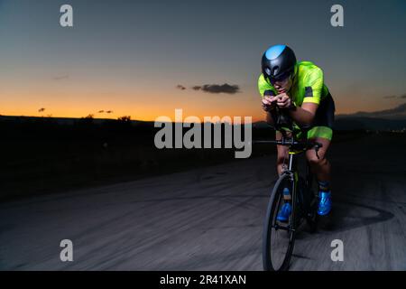 A triathlete rides his bike in the darkness of night, pushing himself to prepare for a marathon. The contrast between the darkne Stock Photo
