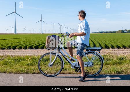 Young man electric green bike bicycle by windmill farm , windmills isolated on a beautiful summer Stock Photo