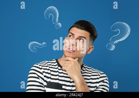 Choice in profession or other areas of life, concept. Making decision, thoughtful man surrounded by drawn question marks on blue background Stock Photo