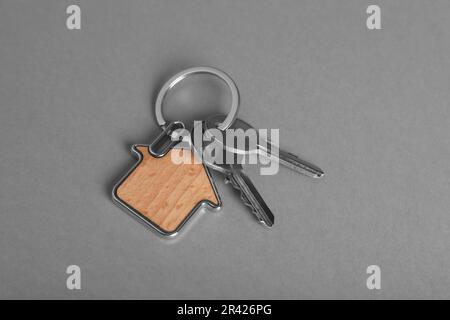 Keys with trinket in shape of house on grey background, above view. Real estate agent services Stock Photo