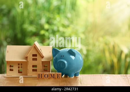 Piggy bank, house model and word Home made of cubes on wooden table outdoors. Space for text Stock Photo