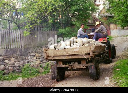 Maramures County, Romania, approx. 2000. Tractor hauling on a village lane a trailer filled with river rocks. Stock Photo