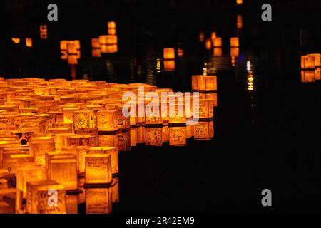 Clump of golden glowing lanterns on black pond at festival Stock Photo