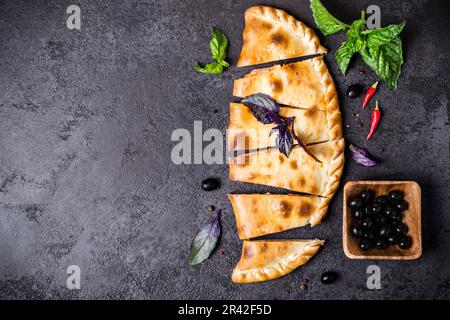 Closed pizza calzone is cut into pieces on black table Stock Photo