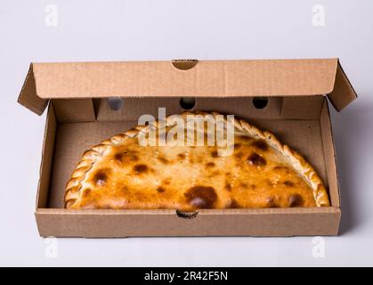 Closed pizza calzone in packing box on gray background Stock Photo