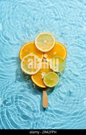 Creative ice lolly made from citrus fruit slices in blue water background with concentric circles and ripples. Refreshing summer Stock Photo
