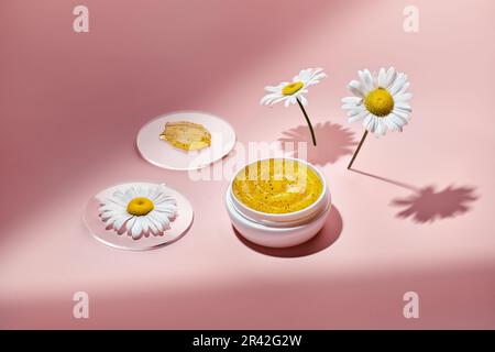 Gel cosmetic product with particles in petri dish on pink background. Natural care cosmetic swatch with chamomile Stock Photo