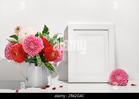 Mockup with photo frame and Autumn dahlias flowers bouquet on white table. Wall table background, trendy shadows Stock Photo
