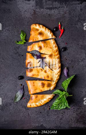 Closed pizza calzone is cut into pieces on black table Stock Photo