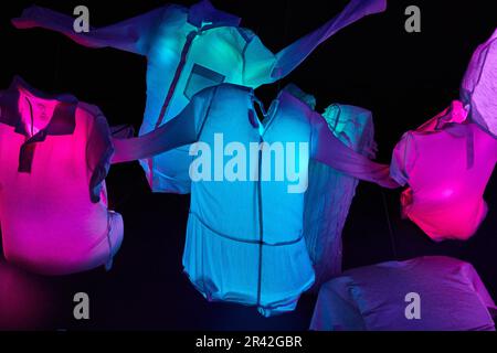 Glowing clothes of neon blue and pink hanging in the air suspended over a black background Stock Photo