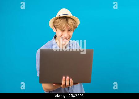 Smiling positive businessman teen holding laptop in hands and typing. Blogger making posts in social networks, chatting with followers. Indoor studio Stock Photo