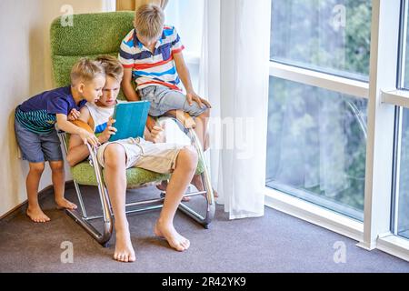 Boys siblings spend time playing interesting games on tablet together. Younger brothers watching preteen schoolboy playing game in hotel room Stock Photo