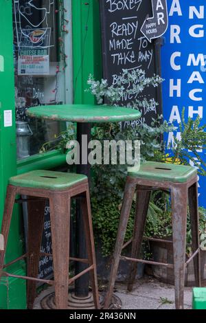 Small round green table and two green stools in front of The Cheese Box, Harbour Street, Whitstable, England. Stock Photo