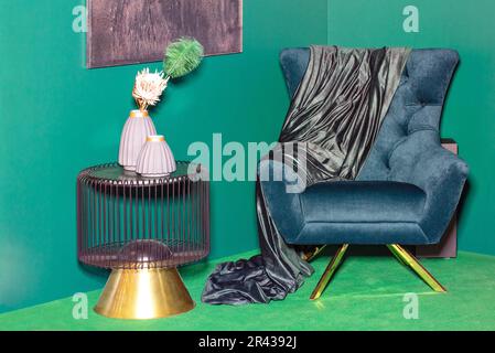 The corner of the living room for relaxation with smooth walls and an easy chair in green tones, a decorative coffee table and earthenware vases. Stock Photo
