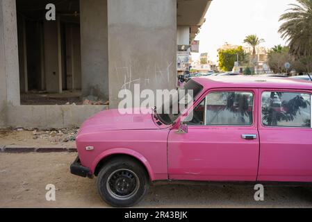 Old used pink car parking in front of a poor building Stock Photo