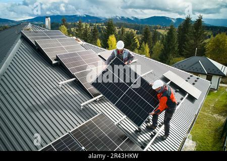 Workers installing solar panels on a roof of house. Solar battery installation in mountains. Concept of alternative energy. Stock Photo