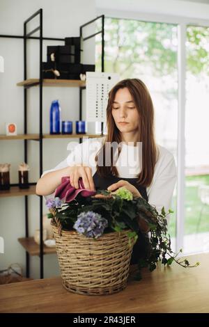 A young woman takes care of flowers. A cheerful florist takes care flowers in a flower shop. Concept of gardening and floristry Stock Photo