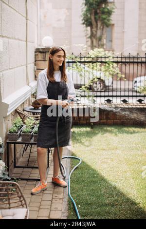 Woman watering fresh herbs growing at home vegetable garden. Gardener taking care of plants at the backyard of her house. Concept of sustainability an Stock Photo