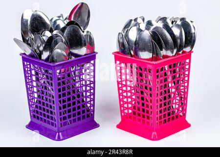Stack of metal spoons in a pink plastic basket isolated on white background Stock Photo
