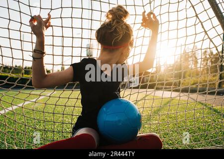 girl sat in a football goal looking away into the distance Stock Photo