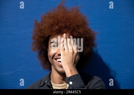 Close up of a happy smiling young man covering one eye with his hand Stock Photo