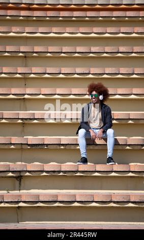 Carefree confident young man sitting alone on a concrete bleacher Stock Photo
