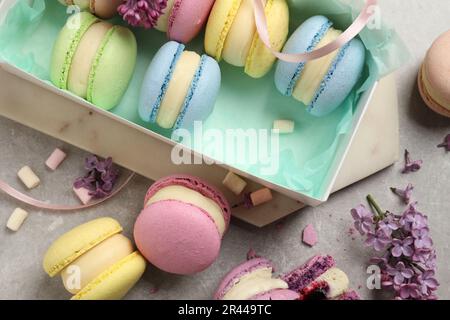 Delicious colorful macarons, marshmallows and lilac flowers on grey table, flat lay Stock Photo