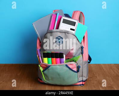 Backpack with different school stationery on wooden floor near light blue wall Stock Photo