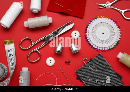 Flat lay composition with thimbles and different sewing tools on red background Stock Photo