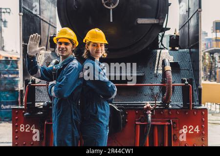 Train engineer team working service maintenance old dirty vintage classic steam engine locomotive in train repair workshop at train station. Stock Photo
