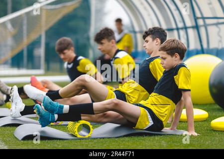 Teenage boys at football training in soccer club. Sports summer camp for youth footballers. Boys using foam therapy rollers after training session out Stock Photo