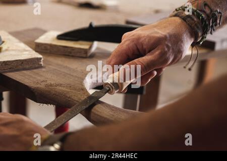 A close-up view of a skilled woodworker's hands meticulously shaping and rounding the wood using a file. Stock Photo