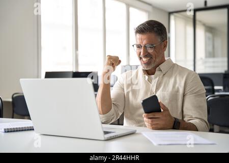 Middle aged man reading great news on smartphone celebrating victory and success Stock Photo
