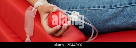 cropped view of multiracial woman with transfusion set and rubber ball sitting on comfortable and ergonomic medical chair while donating blood in hosp Stock Photo