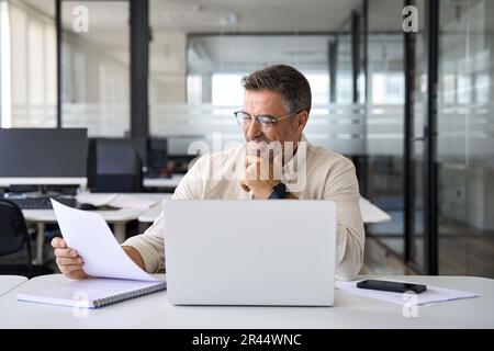 Focused Hispanic businessman doing paperwork in office with copy space. Stock Photo