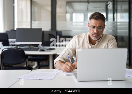 Focused mature Latin businessman working on laptop in office with copy space. Stock Photo