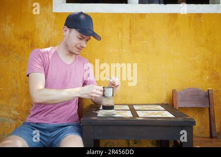 Man enjoying glass of traditional hot Vietnamese coffee with condensed milk. Traveler in Vietnam. Stock Photo